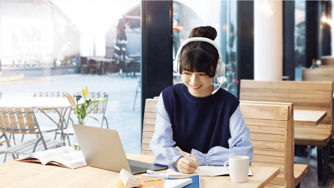 Young woman writing in notebook while looking at PC